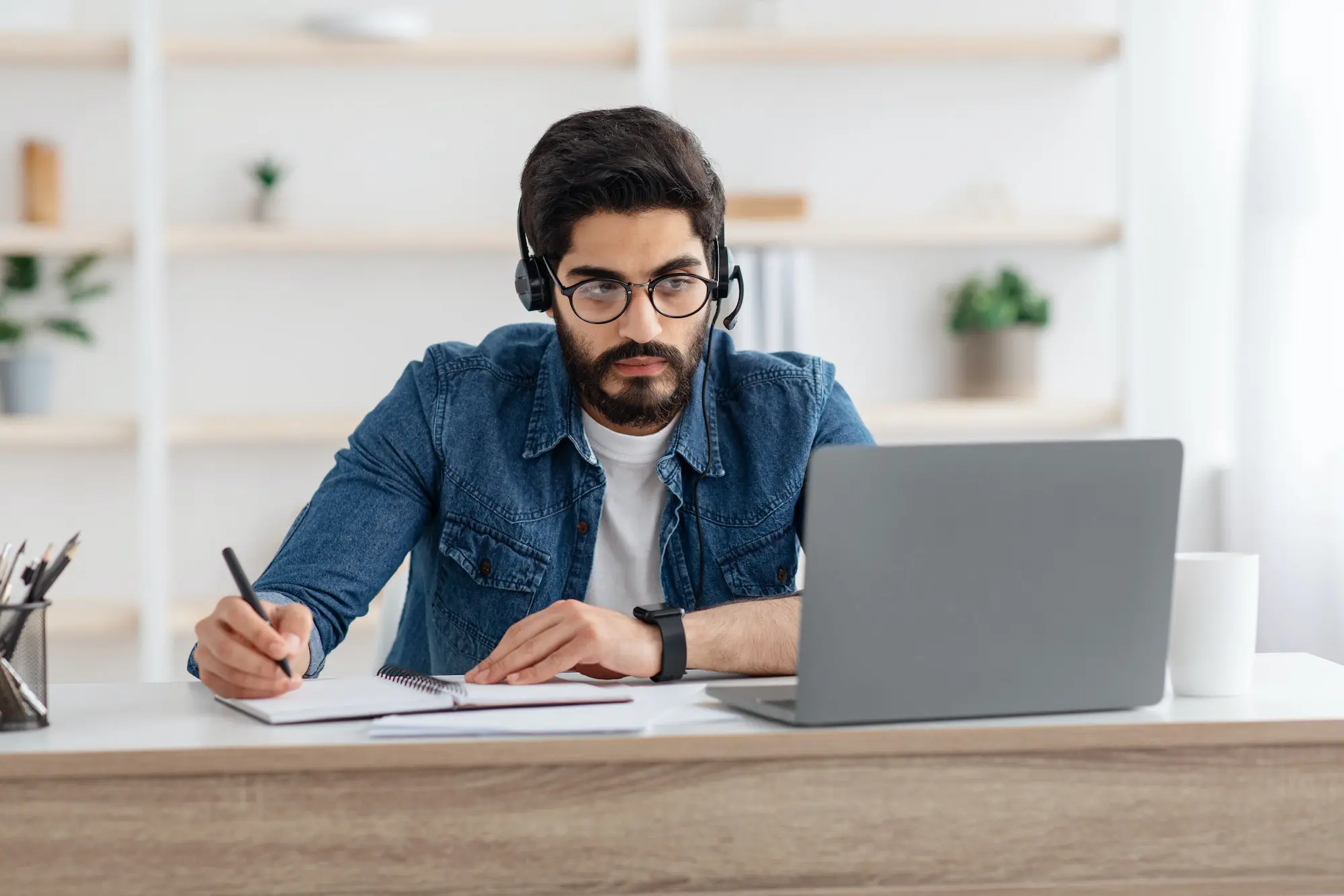 Millennial arab guy in headset watching online webinar on laptop at home, studying with computer and